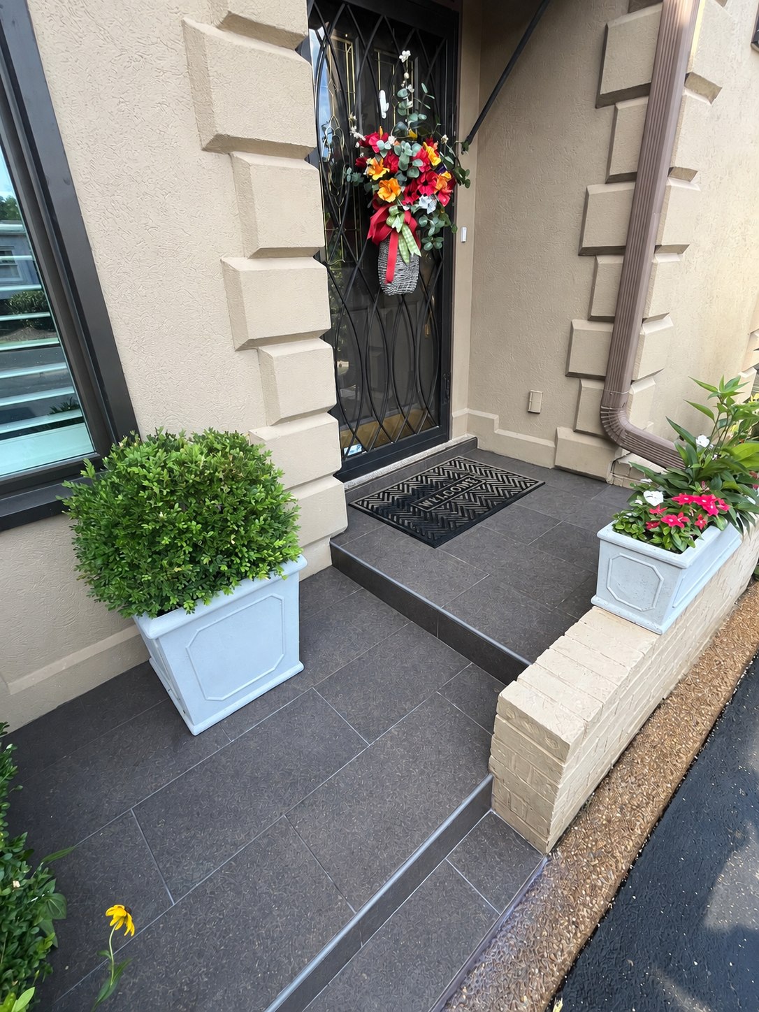 Completed dark tile entryway with a front door and planters
