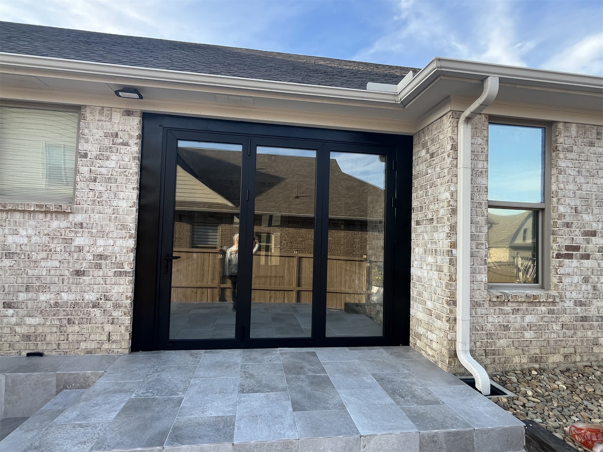 Completed covered entry with black-framed patio doors and light stone tile